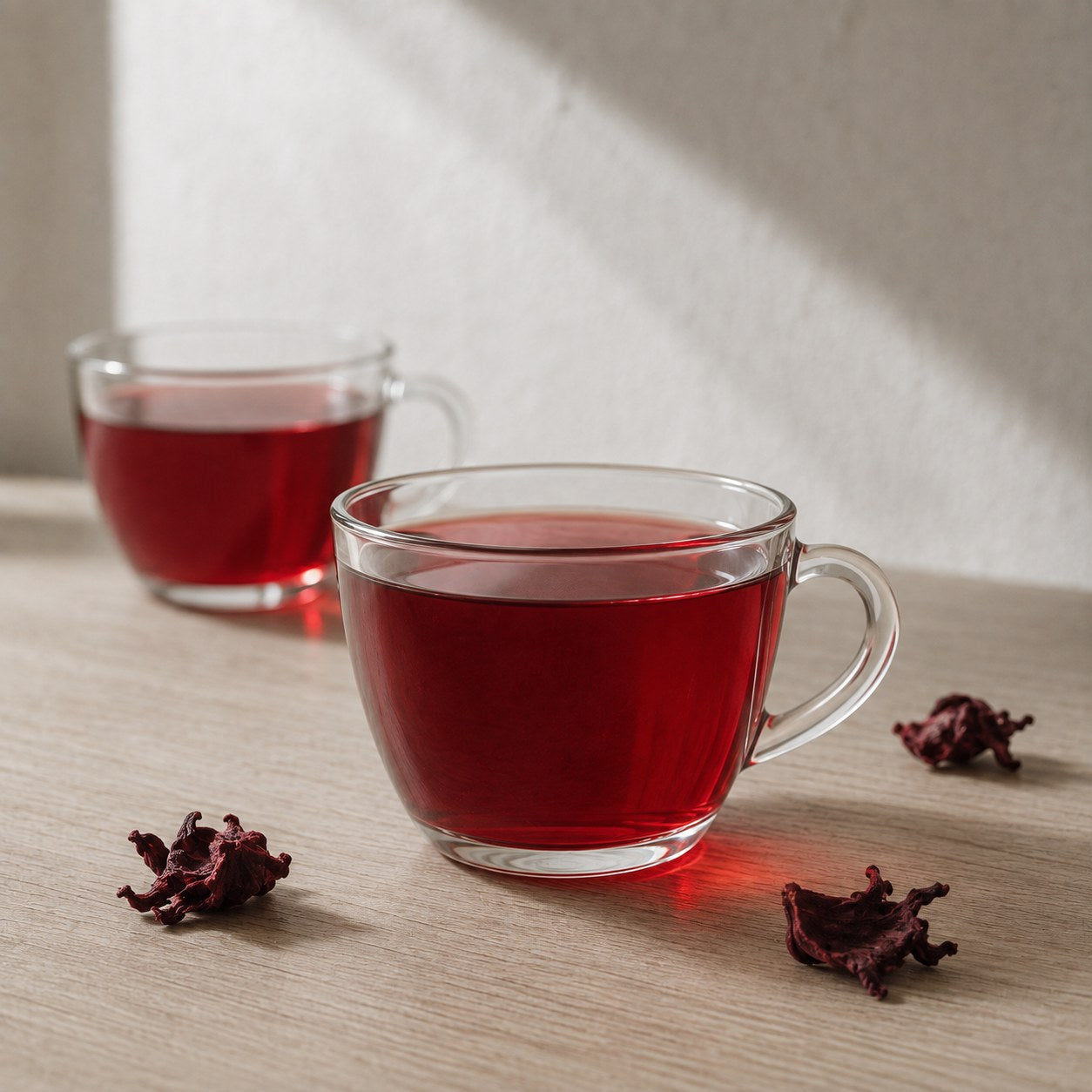 Two glass cups of hibiscus tea beside loose calyces